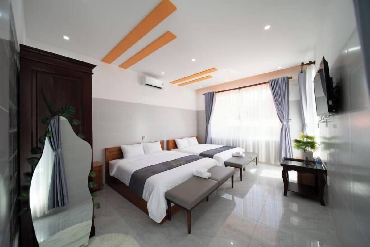 A modern hotel room with two beds, a desk, a TV, and a large window with curtains.