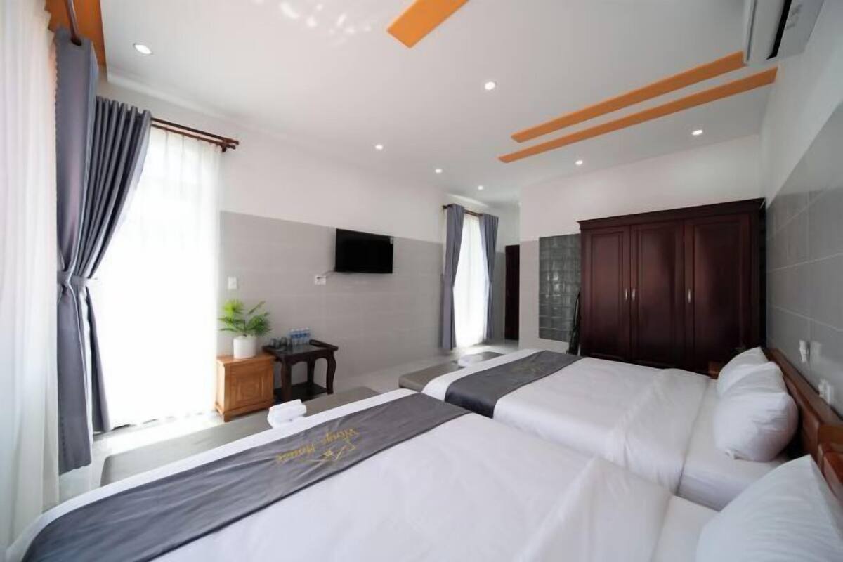 A hotel room with two beds, a TV, a wooden cabinet, and a small table with a plant.