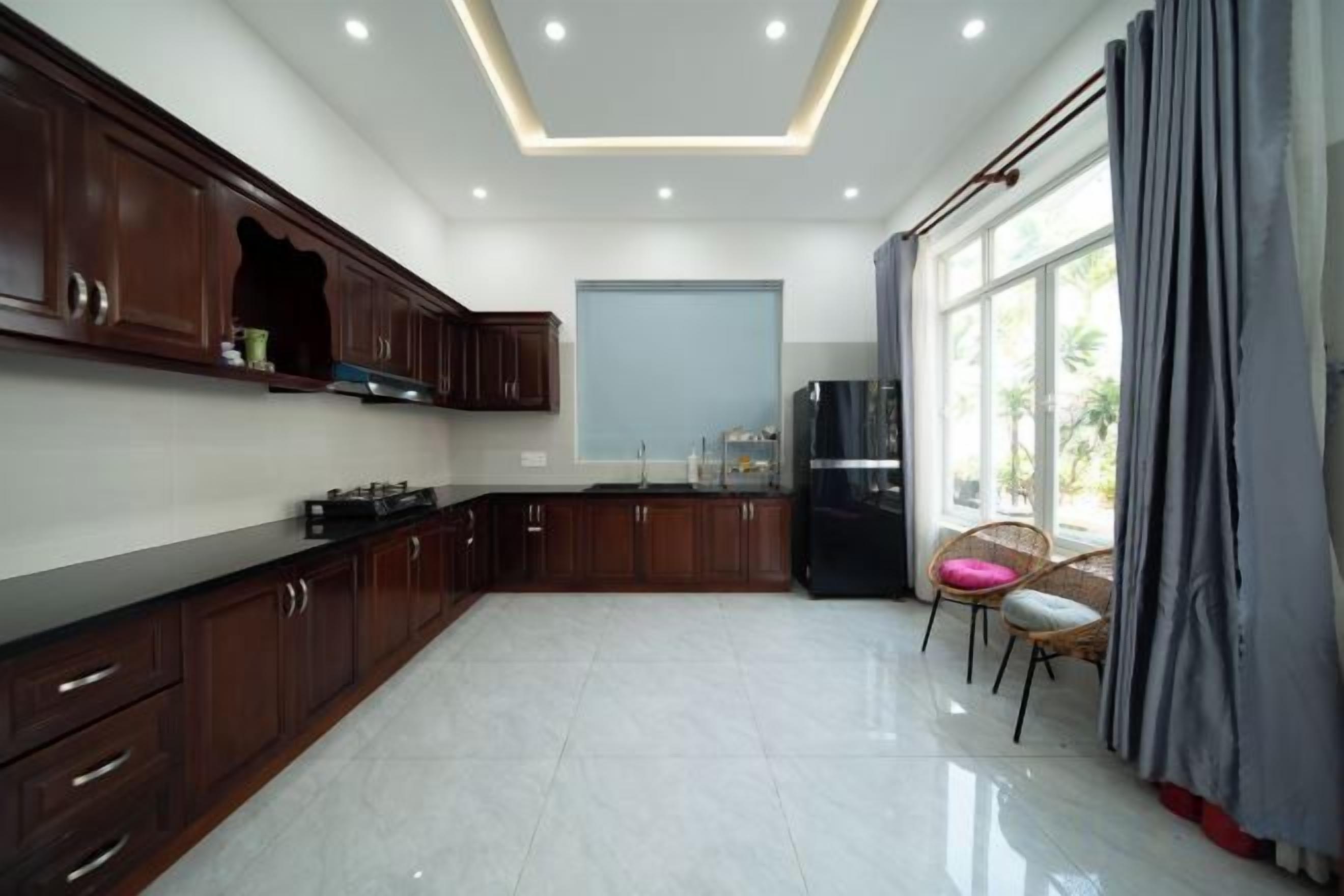 A modern kitchen with dark wooden cabinets, a black refrigerator, and a dining area with two chairs.