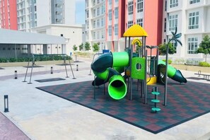 A playground with a slide and climbing structures, surrounded by a checkered floor, in an urban setting with buildings in the background. - Anderson Ipoh by Iconique (Ipoh)