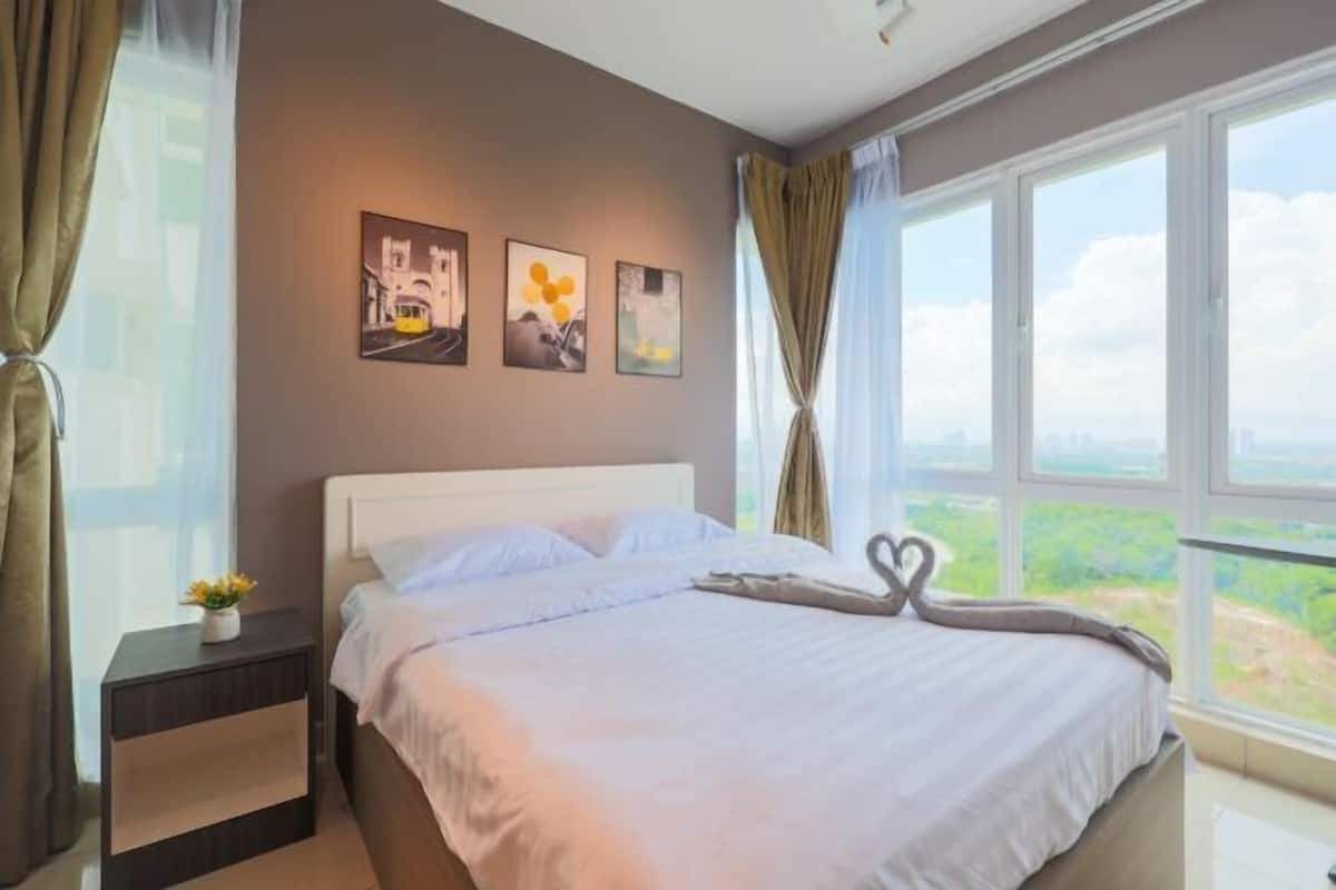 A hotel room with a large bed, a nightstand with a vase, and a cityscape view.