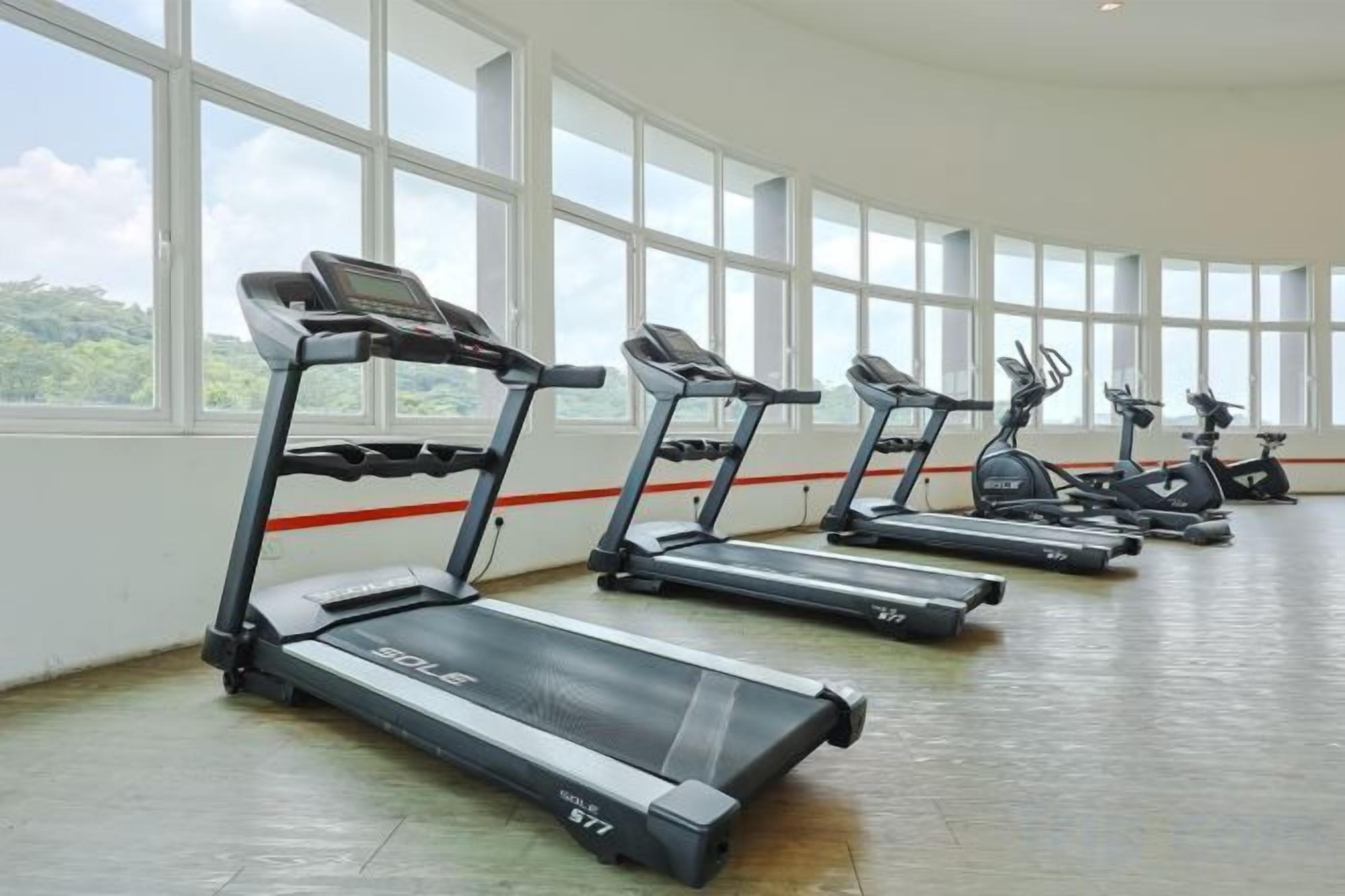 A row of stationary bikes and treadmills in a room with large windows.