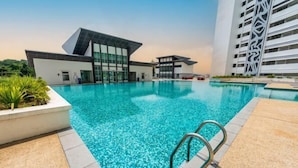 A modern hotel pool area with clear blue water, a contemporary building with large windows, and a patterned pool deck. - Vision Residence By Fei Hong (Puchong)