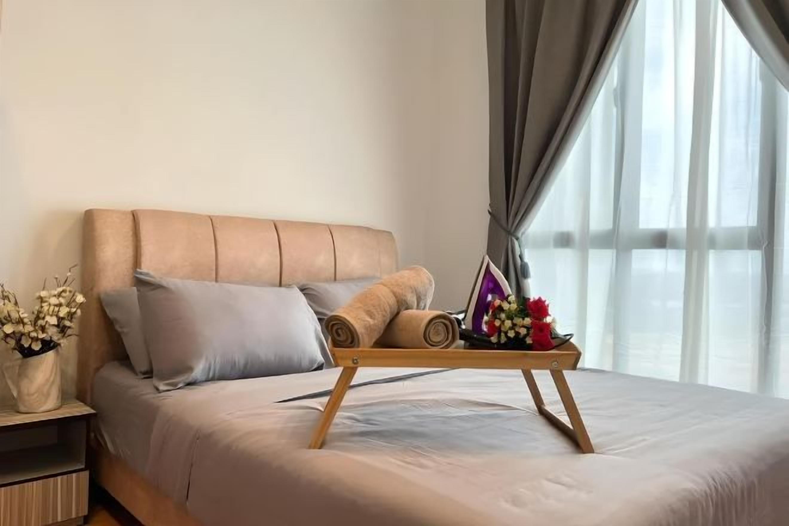 A neatly made bed with a wooden frame, a bedside table with a vase of flowers, and a window with sheer curtains.