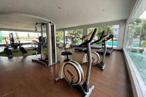 A gym with exercise equipment, a pool visible through the windows, and a wooden floor. - The Platino, Grey Suite by Antlerzone (Tebrau)