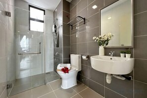 Une salle de bain moderne avec une douche à parois de verre, des toilettes décorées d’un ruban rouge, un lavabo avec un miroir au-dessus et une plante en pot posée sur le comptoir.