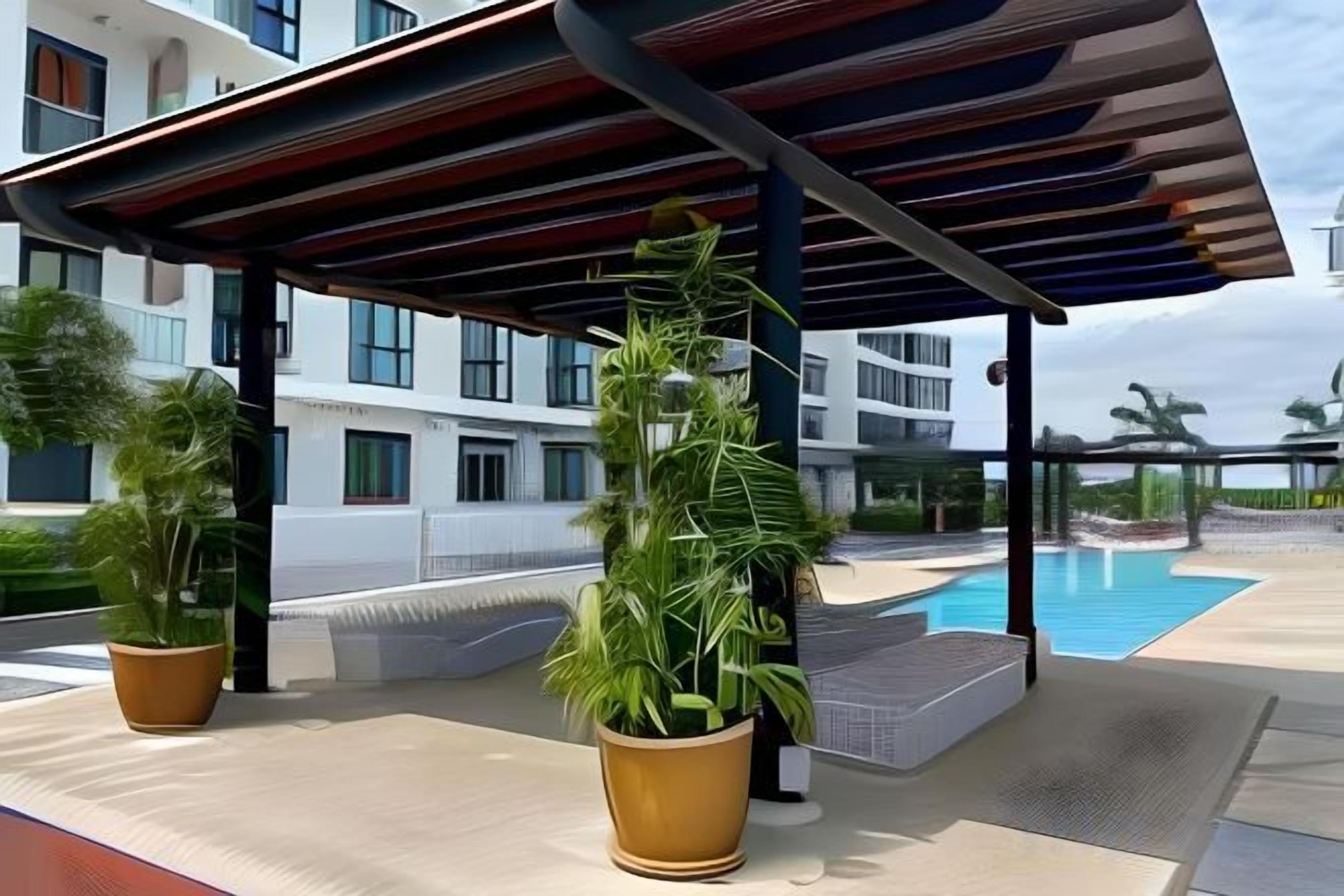 A covered outdoor area with potted plants, a pool, and a building in the background.