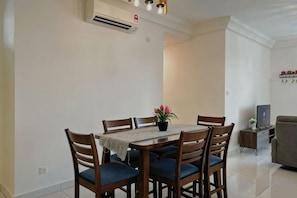 Uma sala de jantar com mesa e cadeiras, um aparelho de ar condicionado e uma televisão ao fundo.