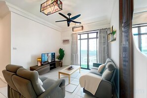 Un salon moderne comprenant un canapé, des fauteuils, une table basse, un téléviseur et un ventilateur de plafond.