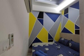 Une chambre avec un lit, un téléphone fixé au mur et un mur orné d’un motif géométrique.