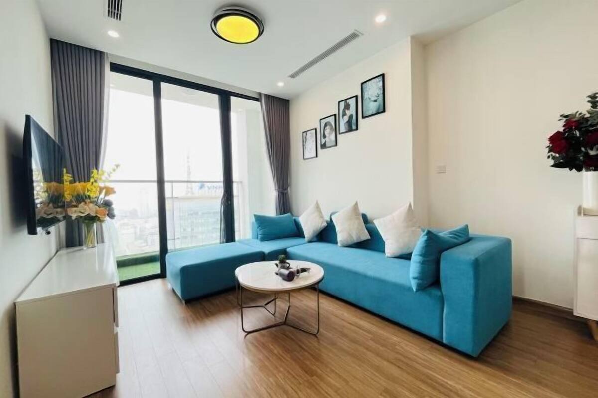Uma sala de estar moderna com um sofá azul, uma mesa redonda pequena e uma janela grande com cortinas.