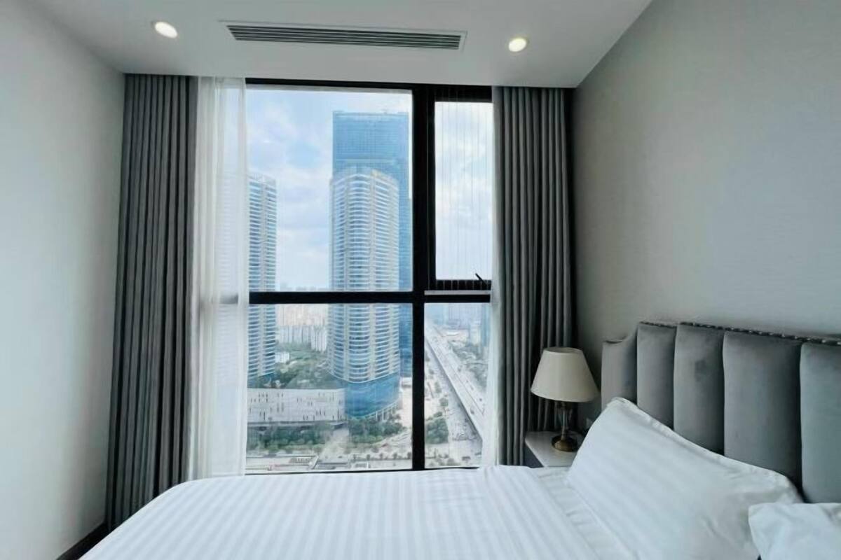 Quarto de hotel com uma janela grande, uma cama, uma mesa de cabeceira e um abajur.