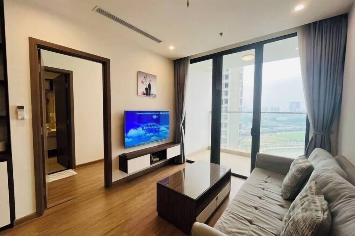 Uma sala de estar moderna com televisão de tela plana, sofá, mesa de centro e uma grande janela com vista para a cidade.