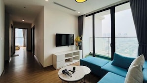 A modern living room with a sofa, a TV, a small table, and a balcony with a city view. - Vinhomes Skylake - Luxury apartment by Sunhouse Land (Hanoi)