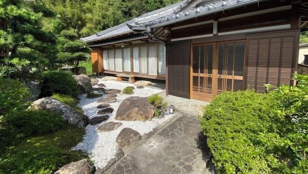 Ein traditionelles japanisches Gebäude mit einem Ziegeldach, hölzernen Schiebetüren und einem Kiesweg zum Eingang.
