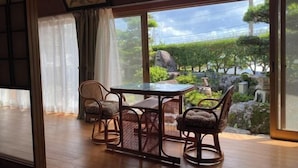 Ein Zimmer mit einem Holztisch und vier Korbstühlen, große Fenster mit Blick auf einen Garten und Felsen.
