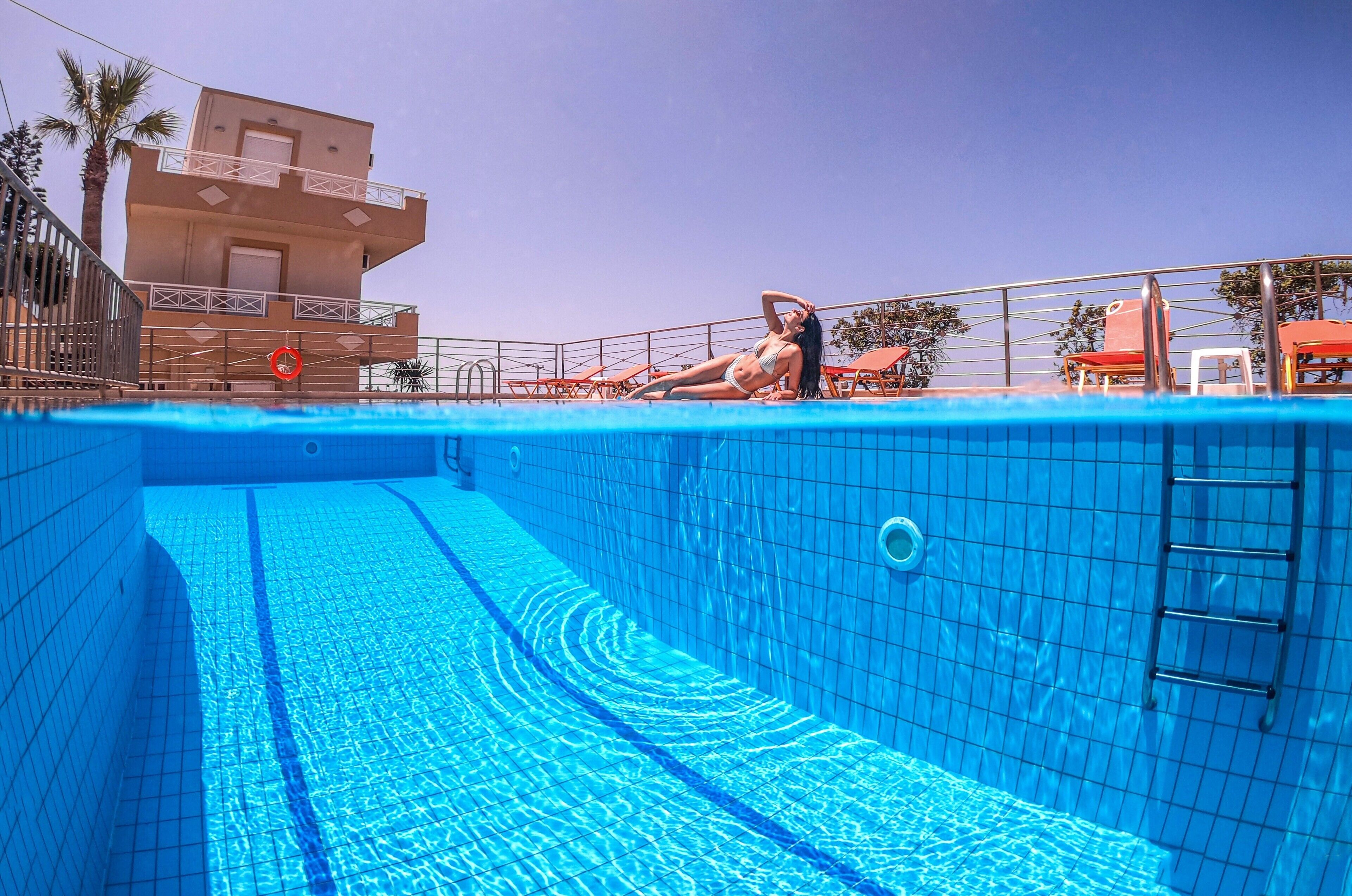 Una piscina con una persona sdraiata sul bordo, una scala e un edificio con un balcone sullo sfondo.