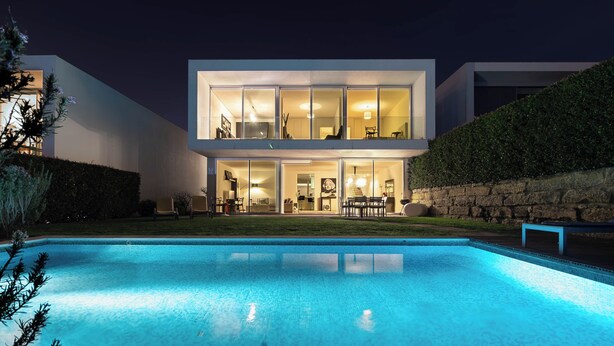 A modern two-story house with a swimming pool in the foreground.
