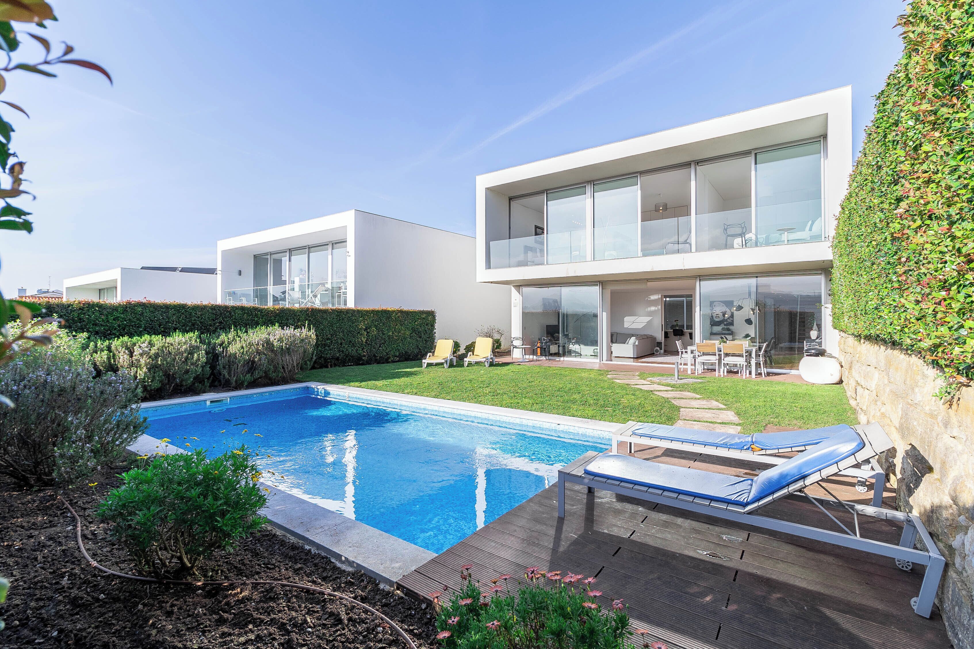 Une maison moderne dotée d’une piscine, de mobilier d’extérieur et d’un jardin bien entretenu.