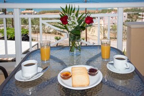 A table with breakfast items, a vase with flowers, and a view of the sea.