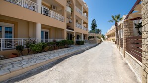 A multi-story hotel with balconies, a paved walkway, and stone walls. - Apartment 'Groundfloor' with Sea View, Wi-Fi and Air Conditioning (Sfakaki)