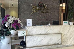 A reception desk with a marble counter, a sign reading 'Botanical Premier,' and a potted plant with white and purple flowers.