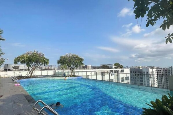 An outdoor swimming pool with clear blue water, surrounded by a high-rise building and trees.