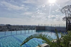 Piscina infinita en la azotea con vistas a la ciudad, rodeada de vegetación.