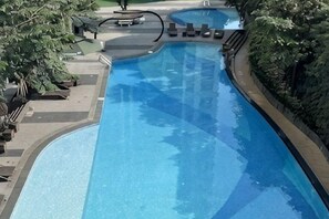 Ein großer, klarer Pool mit geschwungener Kante, umgeben von Grünpflanzen und einigen Liegestühlen.