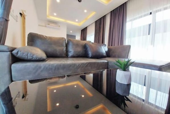 A modern living room with a sofa, a glass coffee table, and a potted plant. - 3 Bedroom Villa Green Mellow-Pattaya (Bang Lamung)