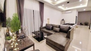 Ein modernes Wohnzimmer mit einer Couch, einem Couchtisch und einem Fernseher. Im Hintergrund befindet sich eine Küchenzeile.