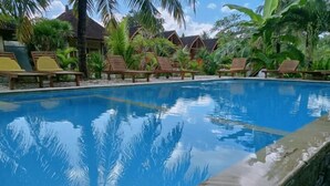 A clear blue pool surrounded by wooden lounge chairs and tropical plants. - Wani Bali Resort 2 (Bali)