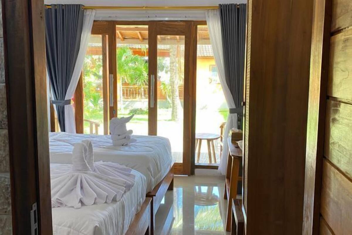 A room with two beds, a small table, and a view of a garden.