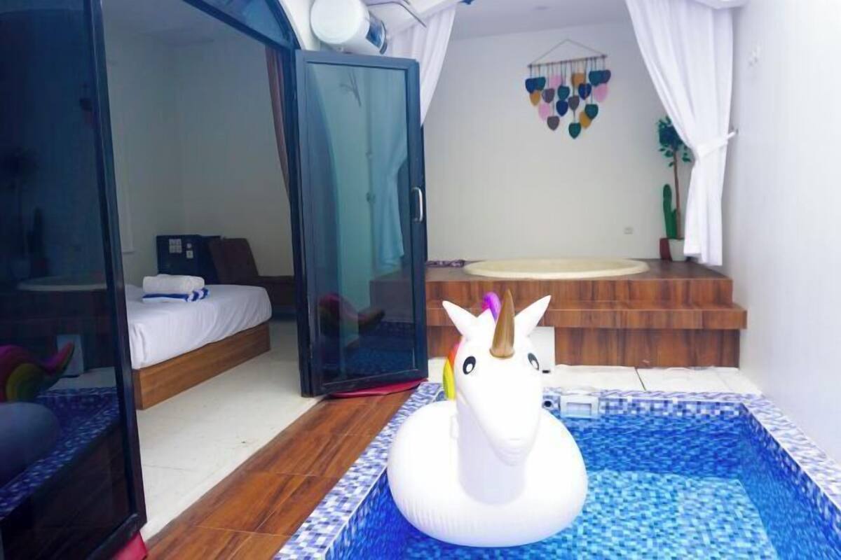 Een slaapkamer met een bed, een glazen deur, een klein zwembadje met een eenhoorn drijvend object en een wanddecoratie.