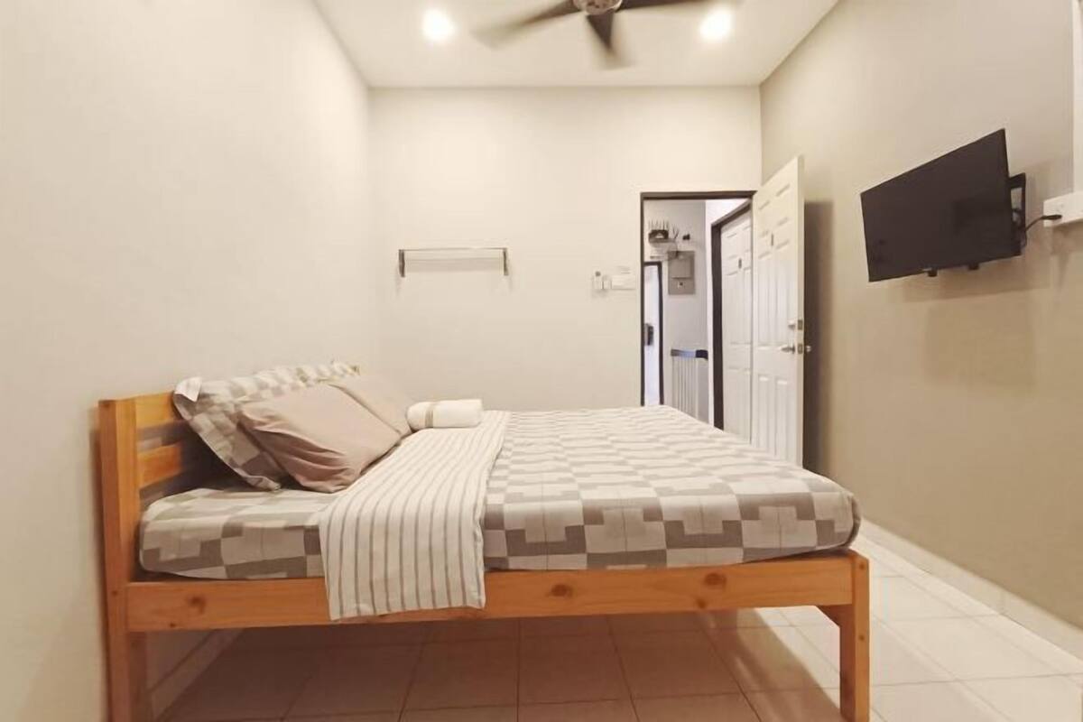 A bedroom with a bed, a ceiling fan, a TV mounted on the wall, and a door leading to another room.
