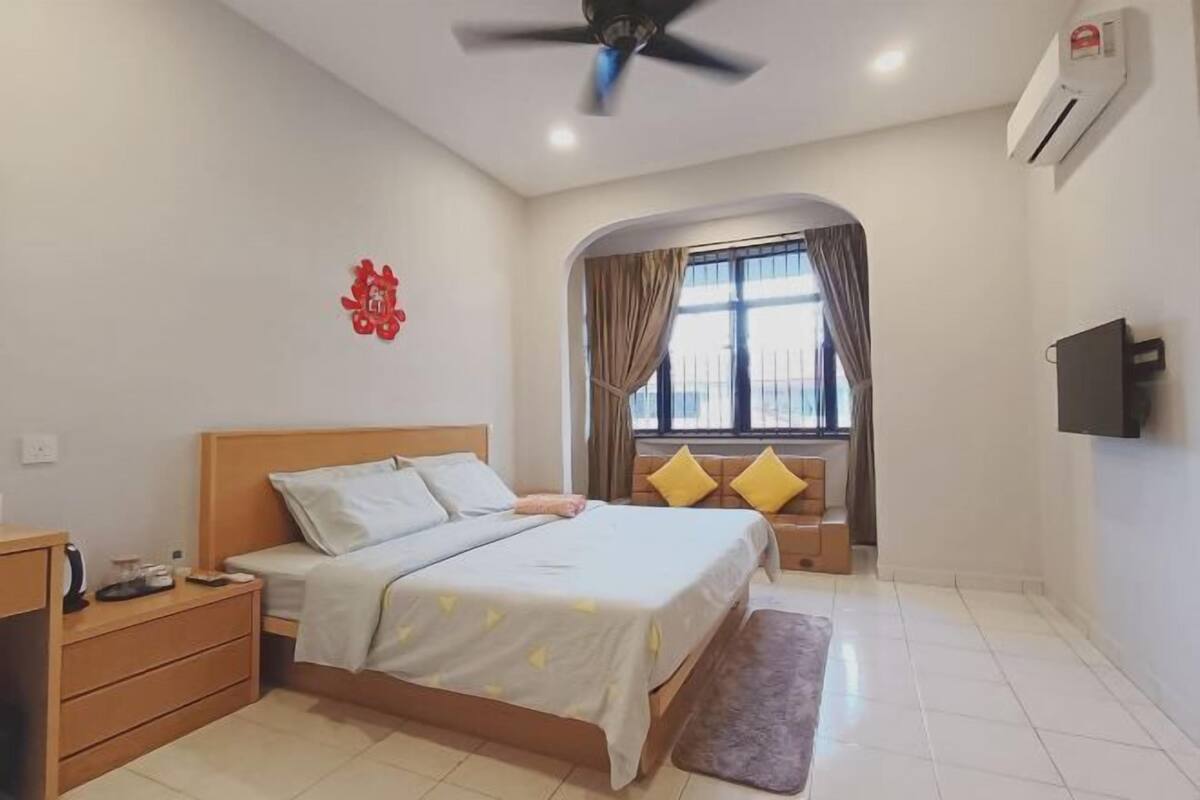 A bedroom with a bed, nightstand, TV, and a window with curtains.