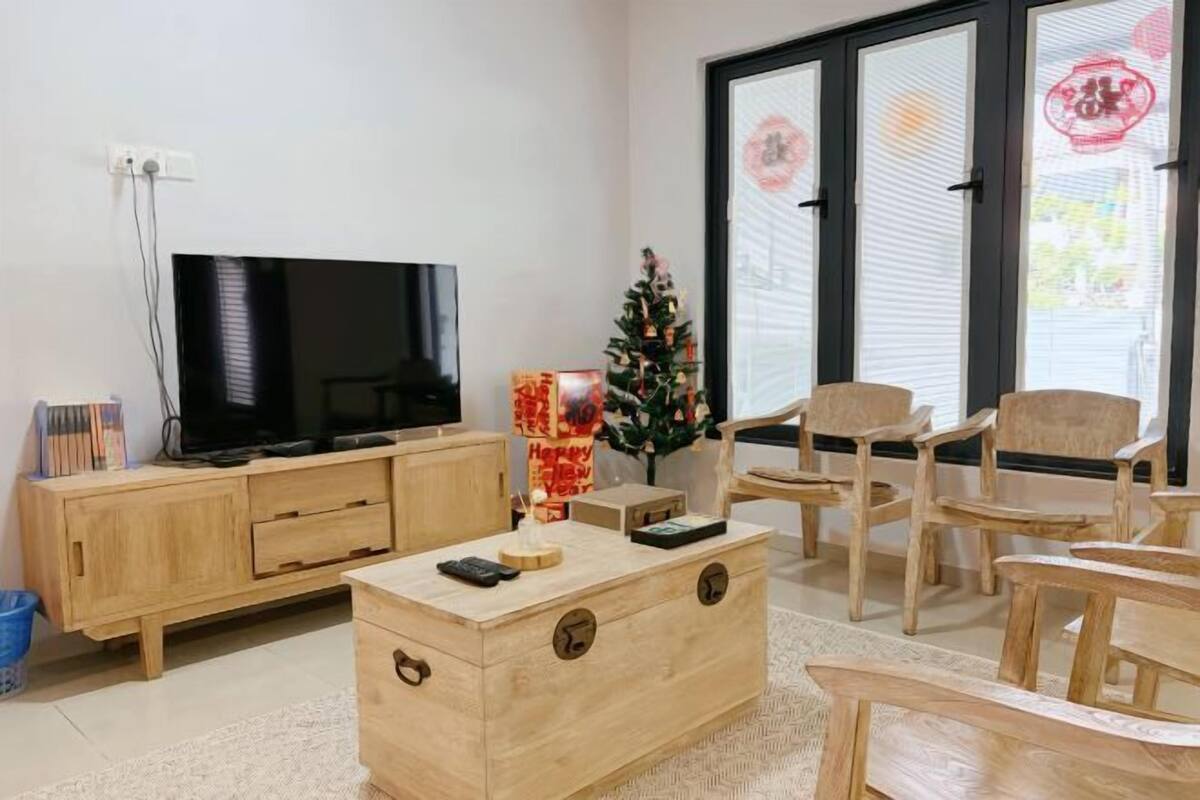 A living room with a TV, wooden furniture, a Christmas tree, and a sliding glass door.