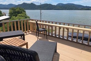 Een houten terras met buitenmeubilair met uitzicht op een meer en bergen.