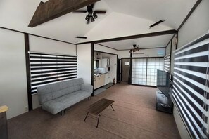 Una sala de estar moderna con un sofá, una mesa de centro y un televisor. Se ve un área de cocina a través de una puerta abierta.