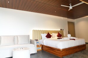 A hotel room with a wooden ceiling, a bed with white bedding and red pillows, a white sofa, and a small round table. - Myrica Groves Lansdowne (Lansdowne)