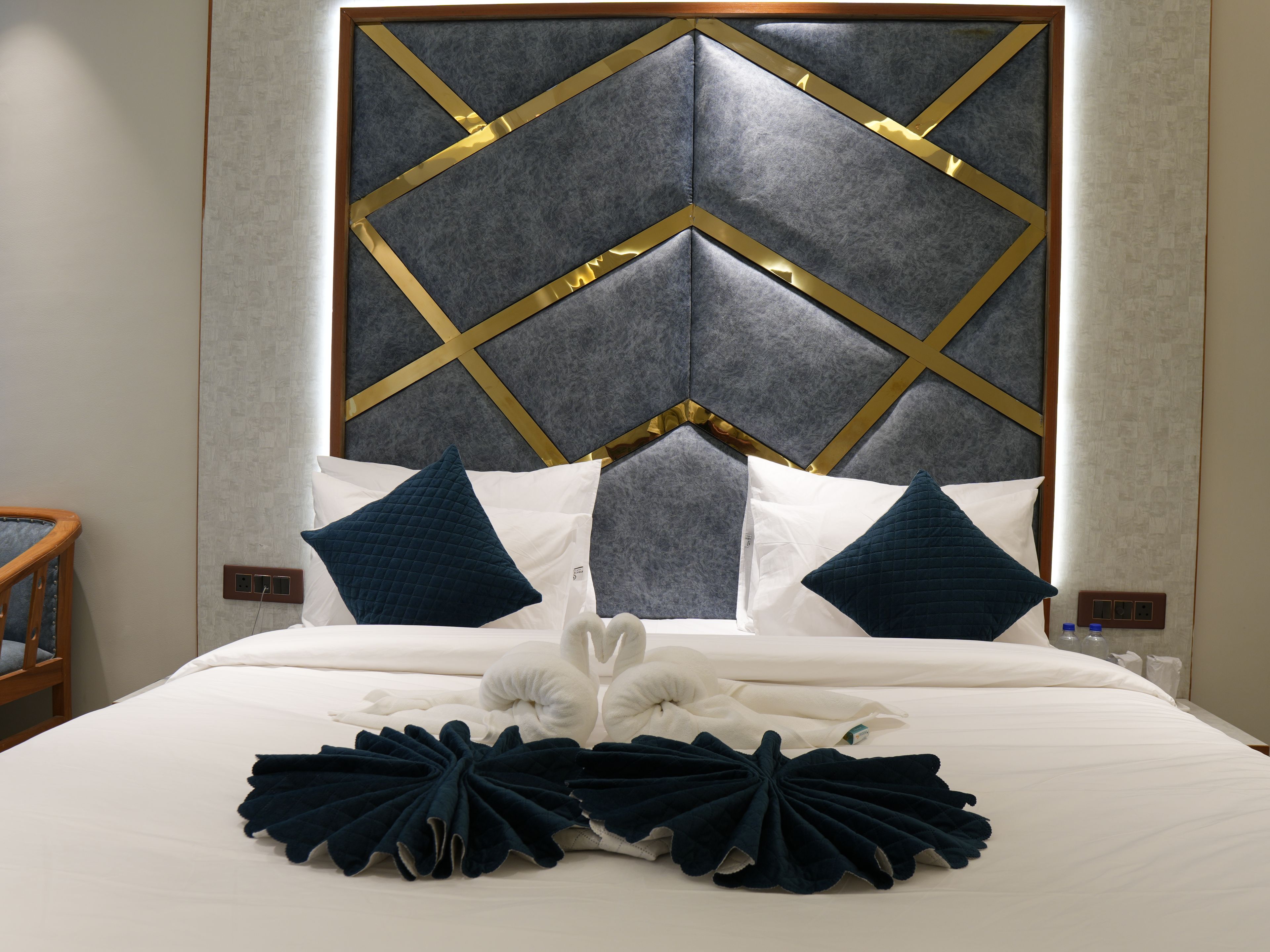 Quarto de hotel com uma cama grande, cabeceira com padrão geométrico e mesa de cabeceira de madeira.