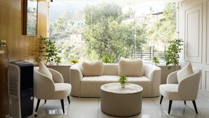 Ein modernes Wohnzimmer mit einer Sofagarnitur, einem Couchtisch und Blick auf eine hügelige Landschaft durch große Fenster.