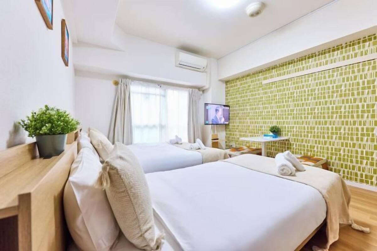 Ein Hotelzimmer mit zwei Betten, einem Fernseher, einem kleinen Tisch und einer Wand mit grünem Muster.