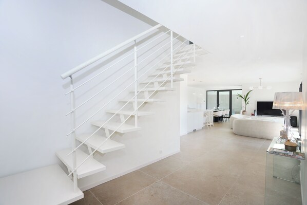 A modern interior with a white staircase, a living area with a sofa, and a dining space. - "Villa Karn veilh" indoor swimming pool, close to the sea and golf course (La Forêt-Fouesnant)