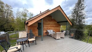 Una cabaña de madera con un porche cubierto, mobiliario exterior y un jardín vallado.