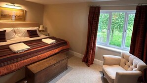 Un dormitorio con cama, una silla, un escritorio, una ventana con cortinas y un cuadro en la pared.