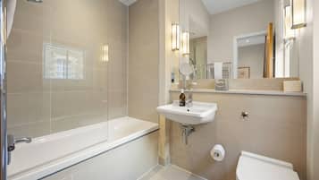 Un baño moderno con ducha envuelta en vidrio, un lavamanos blanco con espejo y un inodoro.