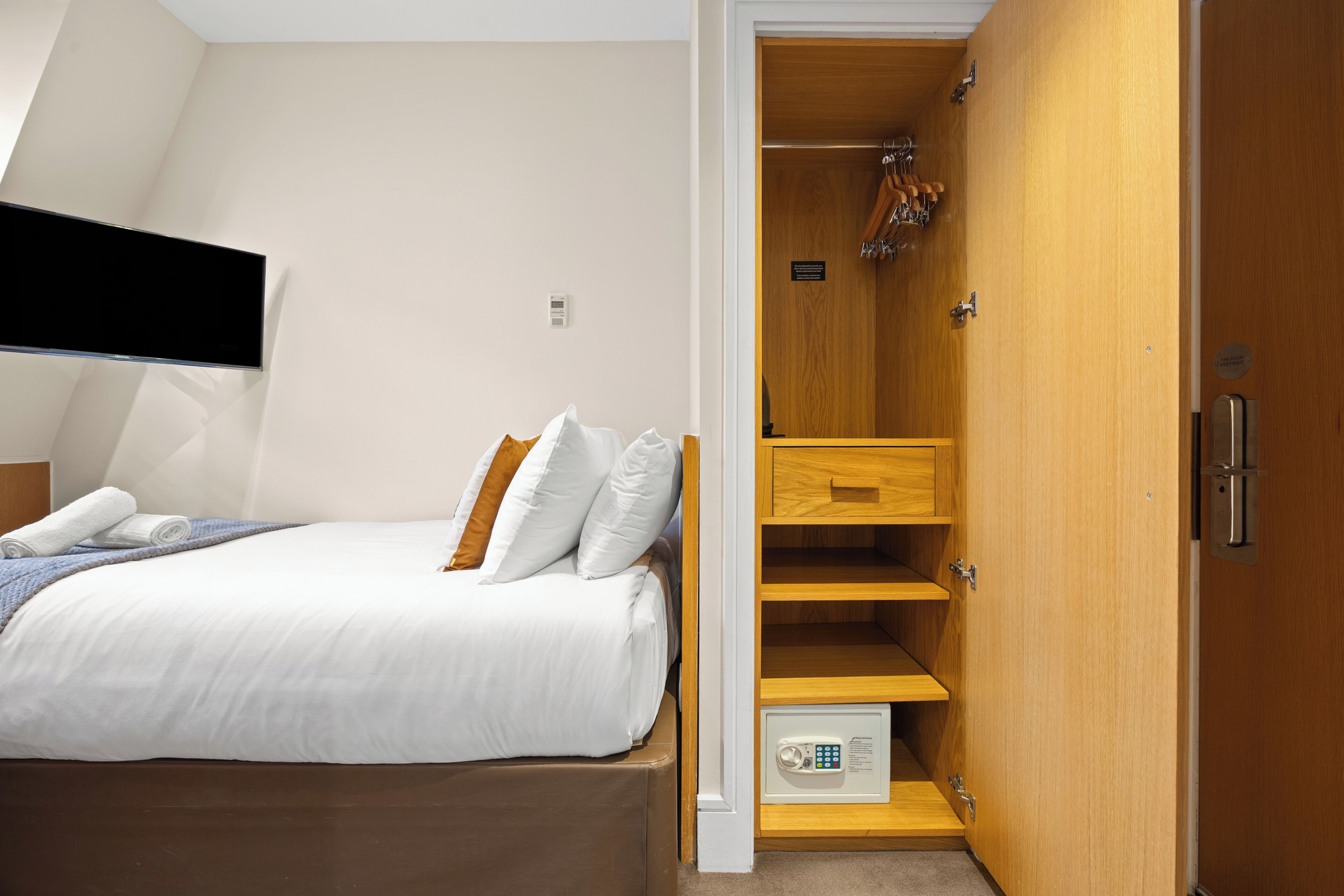 A bedroom with a bed, a wooden wardrobe, and a shower area.