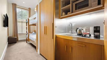 Habitación de hotel compacta con literas, kitchenette y un gran ventanal con persianas.