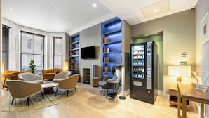 A modern living room with a flat-screen TV, built-in bookshelves, a refrigerator, and seating arrangements. - Kula London Kensington (London)
